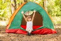 Happy child girl in sunglasses enjoy summer time with hands up in camping tent in summer forest Royalty Free Stock Photo