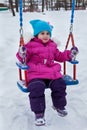 Happy child girl on swing in sunset winter. Little kid playing on a winter walk in nature