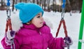 Happy child girl on swing in sunset winter. Little kid playing on a winter walk in nature