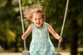 Happy child girl on swing on warm and sunny day outdoors. Little kid playing on nature walk in playground in park, cute blond girl Royalty Free Stock Photo