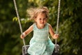 Happy child girl on swing on warm and sunny day outdoors. Little kid playing on nature walk in playground in park, cute blond girl Royalty Free Stock Photo