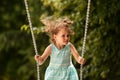 Happy child girl on swing on warm and sunny day outdoors. Little kid playing on nature walk in playground in park, cute blond girl Royalty Free Stock Photo