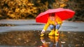 Happy child girl with umbrella and paper boat in puddle in a Royalty Free Stock Photo