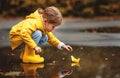 Happy child girl with umbrella and paper boat in puddle in a Royalty Free Stock Photo