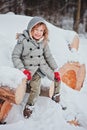 Happy child girl on the walk in snowy winter forest sitting on wood log
