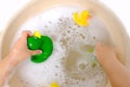 happy child, girl 3 years old plays with rubber green, yellow ducks for swimming, child's toy in soapy foam Royalty Free Stock Photo