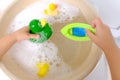 Happy child, girl 3 years old plays with rubber green, yellow ducks for swimming, plastic boat, child`s toys in soapy foam, Royalty Free Stock Photo