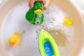 Happy child, girl 3 years old plays with rubber green, yellow ducks for swimming, plastic boat, child`s toys in soapy foam, Royalty Free Stock Photo