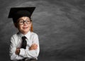 Happy Child in Glasses and Graduation Hat thinking over Blackboard. Cheerful smiling Preschool Boy in Eyeglasses over Chalkboard. Royalty Free Stock Photo