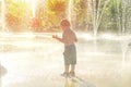 Happy child has fun playing in water fountains on hot day during summer. Boy playing in water at waterpark. A kid in spray park Royalty Free Stock Photo