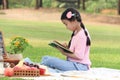 Happy child has a picnic in summer park, cute Asian girl reading book and studying outside while sitting on mat on green grass. Royalty Free Stock Photo