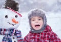 Happy child having fun and playing with snowmen in winter snowy day. Portrait of three years old smiling trendy hipster boy kid.