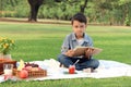 Happy child having a picnic in summer park, cute Asian boy reading book and studying outside while sitting on mat on green grass. Royalty Free Stock Photo