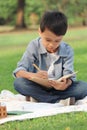 Happy child having a picnic in summer park, cute Asian boy reading book and studying outside while sitting on mat on green grass. Royalty Free Stock Photo