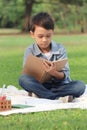 Happy child having a picnic in summer park, cute Asian boy reading book and studying outside while sitting on mat on green grass. Royalty Free Stock Photo