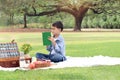 Happy child having a picnic in summer park, cute Asian boy reading book and studying outside while sitting on mat on green grass. Royalty Free Stock Photo