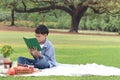 Happy child having a picnic in summer park, cute Asian boy reading book and studying outside while sitting on mat on green grass. Royalty Free Stock Photo