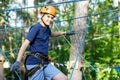 Happy child, healthy teenager in helmet enjoys activity in a climbing adventure rope park