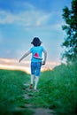 Happy child, holding pair of sneakers in hands, walking on a rural path