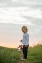 Happy child, holding pair of sneakers in hands, walking on a rural path