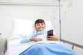 Happy child in hospital bed using smartphone surfs the internet wearing earphones