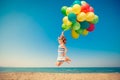 Happy child jumping with colorful balloons on sandy beach