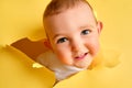 A happy child looks out of a hole in the studio yellow background. Smil Royalty Free Stock Photo