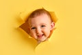 A happy child looks out of a hole in the studio yellow background. Smil Royalty Free Stock Photo