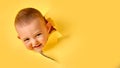 A happy child looks out of a hole in the studio yellow background. Smil Royalty Free Stock Photo