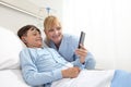 Happy child lying in bed in hospital room and smiling nurse using smartphone surfs the internet wearing earphones