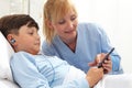 Happy child lying in bed in hospital room and smiling nurse using smartphone surfs the internet wearing earphones