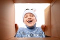 A happy child in a new year`s hat and a warm knitted sweater opens a new year`s gift, a view from inside the box