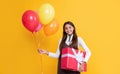 happy child with party helium balloons and present box on yellow background