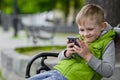 Happy child play cell, smart phone, sitting on a city bench Royalty Free Stock Photo