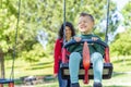 Happy Child playing on outdoor playground with his mom. Kids play on school or kindergarten yard. Active kid on colorful swing. Royalty Free Stock Photo