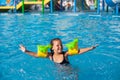 Happy child is playing in pool. Little girl in inflatable armbands with dinosaurs is happy from swimming lessons in new