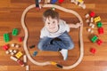 Happy child playing with toys. Boy sitting on wooden floor ant looking up at camera and smiling.