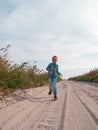 Happy child running jumping having fun on empty autumn beach. Blond girl walking on white sand road