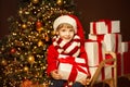 Happy Child in Santa Hat holding Gift. Stack of Xmas Presents on Christmas tree Lights Background Royalty Free Stock Photo