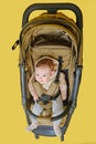 A happy child is sitting in a baby carriage on a studio yellow background. Smiling toddler baby boy in a transformer stroller for