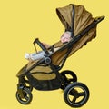 A happy child is sitting in a baby carriage on a studio yellow background. Smiling toddler baby boy in a transformer stroller for
