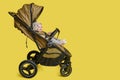 A happy child is sitting in a baby carriage on a studio yellow background. Smiling toddler baby boy in a transformer stroller for