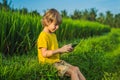 Happy child sitting on the field holding tablet. Boy sitting on the grass on sunny day. Home schooling or playing a Royalty Free Stock Photo