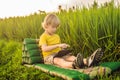Happy child sitting on the field holding tablet. Boy sitting on the grass on sunny day. Home schooling or playing a Royalty Free Stock Photo