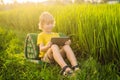 Happy child sitting on the field holding tablet. Boy sitting on the grass on sunny day. Home schooling or playing a Royalty Free Stock Photo