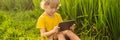 Happy child sitting on the field holding tablet. Boy sitting on the grass on sunny day. Home schooling or playing a Royalty Free Stock Photo