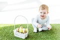 Child sitting near straw basket with colorful Easter eggs isolated on white