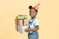 happy child smiling african girl, wearing birthday hat and casual jeans overalls, holding stack og colorful gift boxes Royalty Free Stock Photo