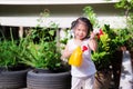 Happy child stand with red and yellow watering can in the little garden at front of her house. Asian cute girl are smiling sweetly Royalty Free Stock Photo