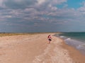 Happy child in a straw hat running jumping having fun on empty autumn sea beach. Blond girl walking on white sand Royalty Free Stock Photo